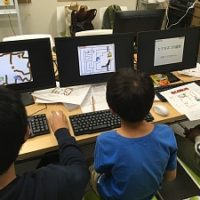 プログラミング教室で、互いにプログラミングしたダンジョンゲームを遊んでいる3人の小学生の男の子